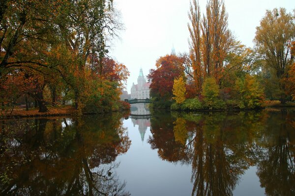 Jesienny krajobraz z rzeką obok której widać most i wysoki budynek