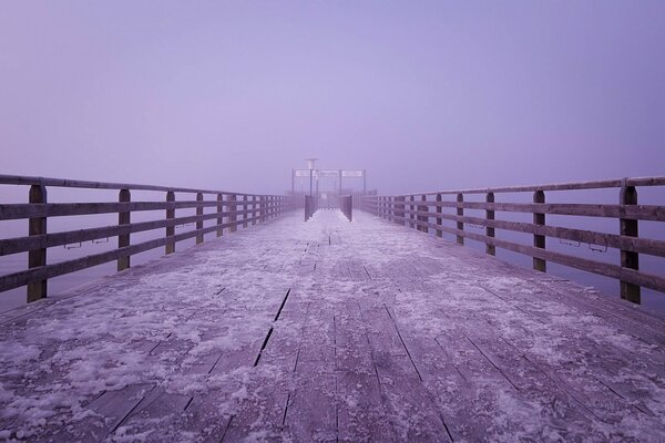 La niebla lila cae sobre un puente de madera cubierto de nieve