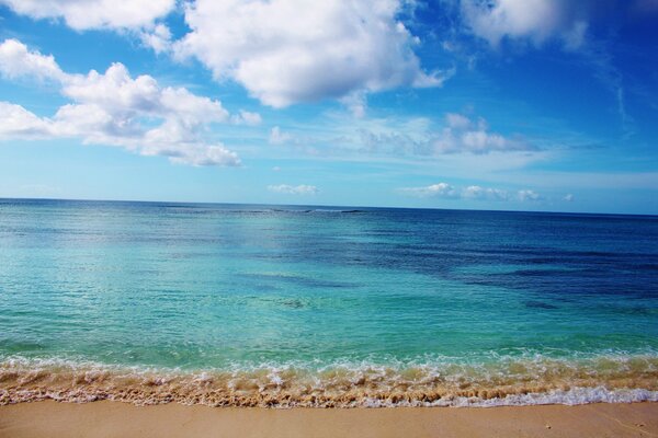 The waves of the blue sea merge with the white clouds