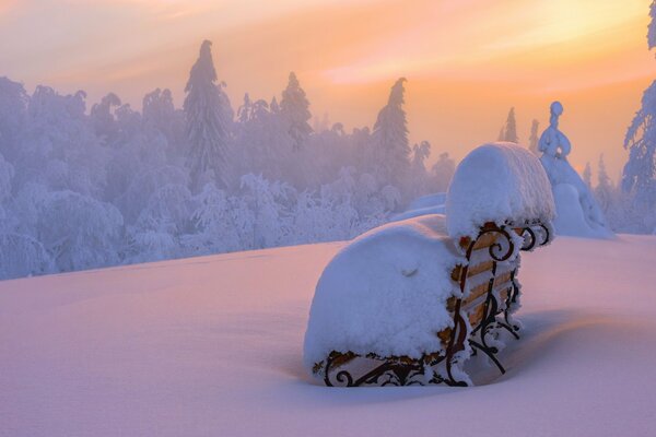 Eine schneebedeckte Bank in Schneewehen und vor dem Hintergrund eines schneebedeckten Waldes