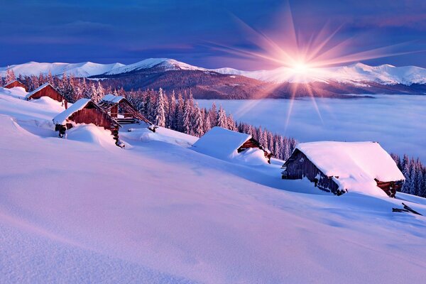 Amanecer en las montañas con casas en la nieve en la ladera