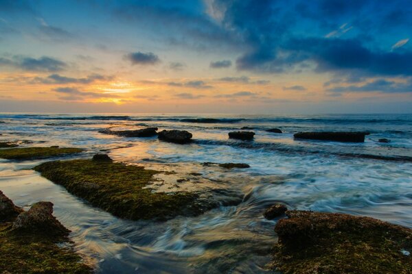 Waves crashing against rocks and the sun making its way through the clouds