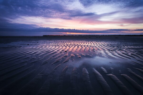 Plage avec des dunes à marée basse sur fond de ciel nuageux coucher de soleil