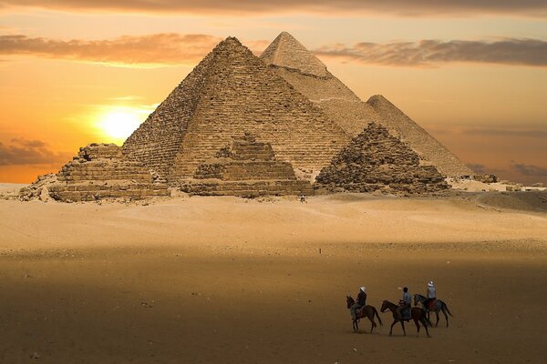 Obraz jasnożółtej piramidy na tle zachodu Słońca, jeźdźcy na pustyni