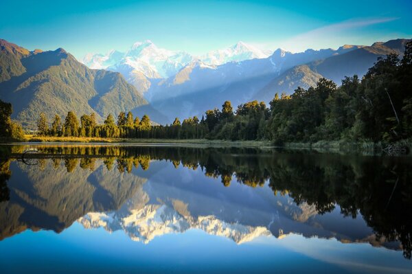 Las montañas y el bosque se reflejan en la superficie azul del agua