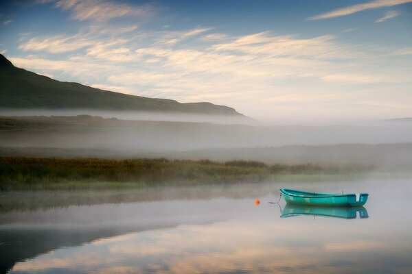 Turquoise boat on the lake on a foggy morning