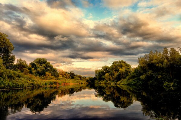 Image of a lake near a dense forest in summer in cloudy weather