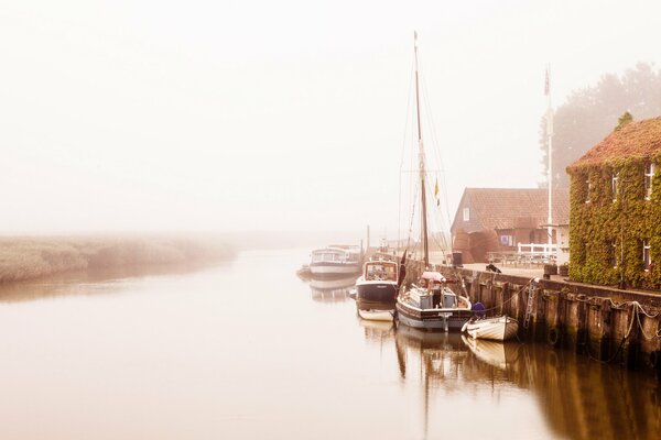 Muelle con barcos en la orilla del río en la niebla