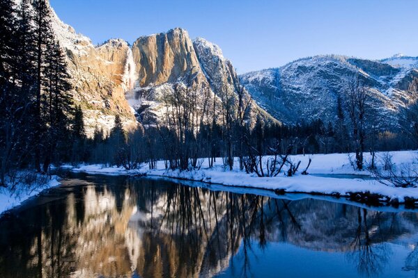 In the winter forest, a stream runs against the background of mountains