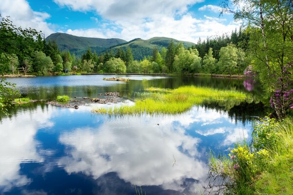 White clouds reflected in the lakes of Scotland on the background of green trees