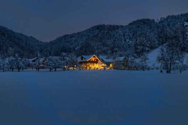 A house in the forest in front of the mountains in winter in snow and lights