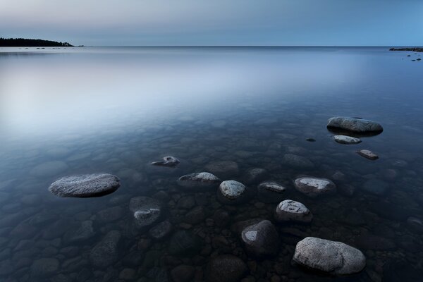 A smooth surface of water with rocks visible through it