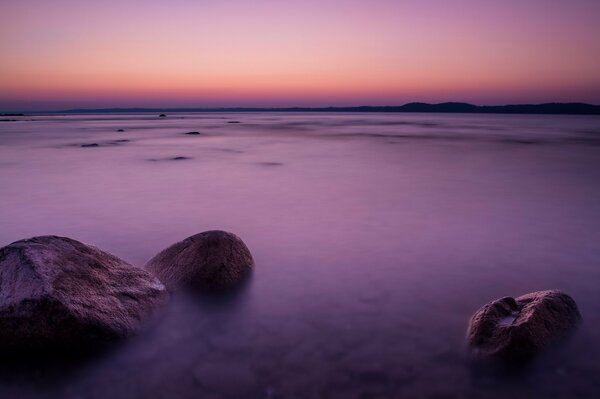 Liliowy Zachód słońca nad morzem z kamieniami