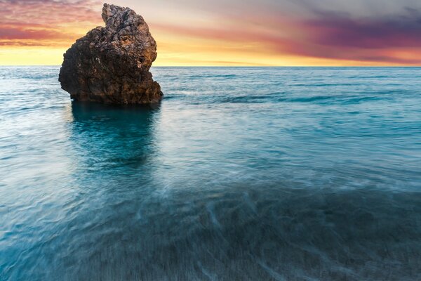 Amanecer sobre una roca solitaria en el océano