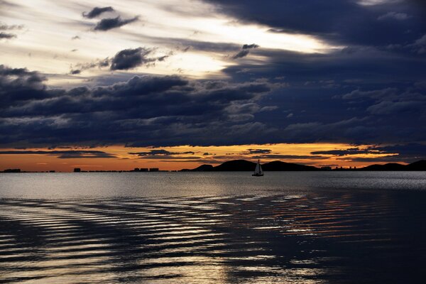 The ship sails on the lake against the background of clouds