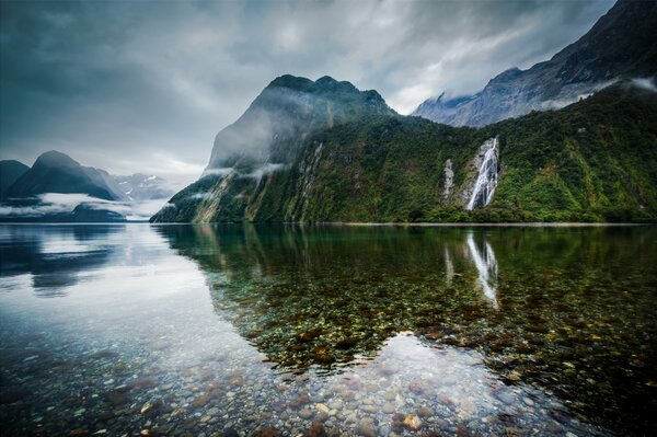 New Zealand. A lake surrounded by mountains with waterfalls, with clear water through which the bottom can be seen