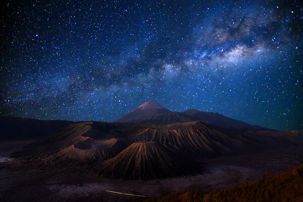 Indonesia, there is a volcano on the island, and above it a beautiful starry sky