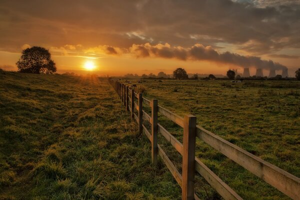 Закатное солнце над полем с забором