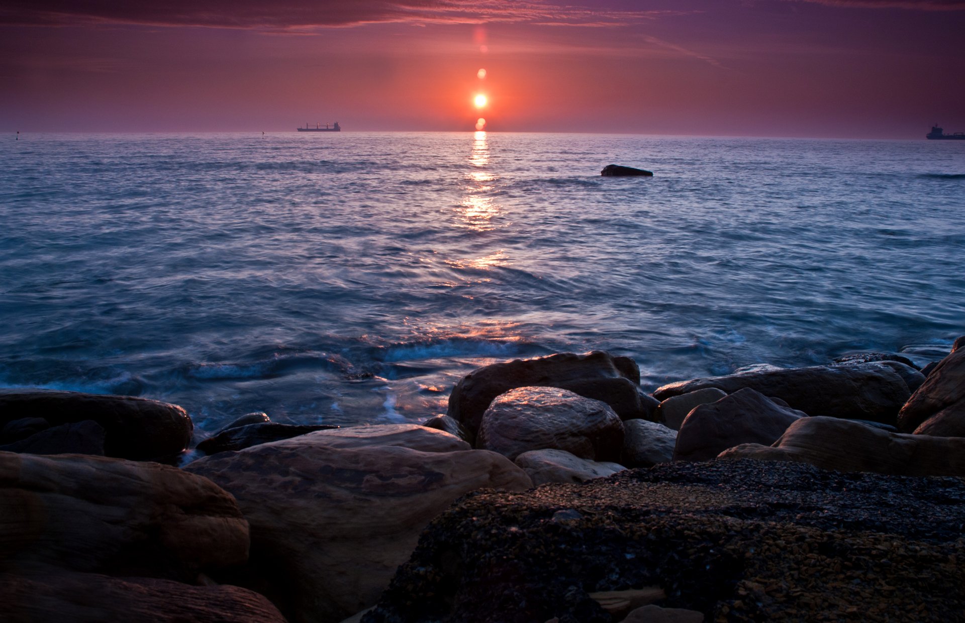 puesta de sol mar piedras barcos