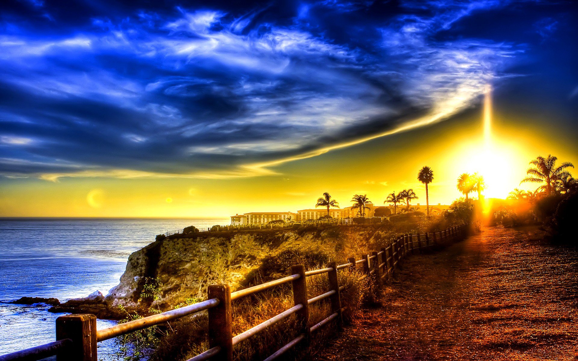 mare oceano costa edifici strada recinzione palme cielo nuvole alba tramonto raggi luce