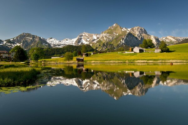 Eine grüne Wiese und ein See, in dem sich die Berge widerspiegeln