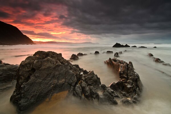 Puesta de sol roja sobre el mar con piedras