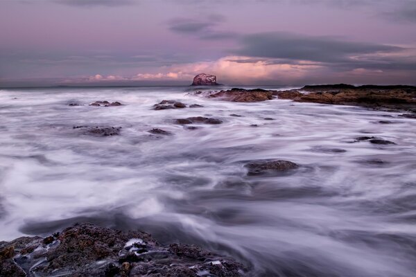 Under a gray sky, the sea surf rolls on the rocks