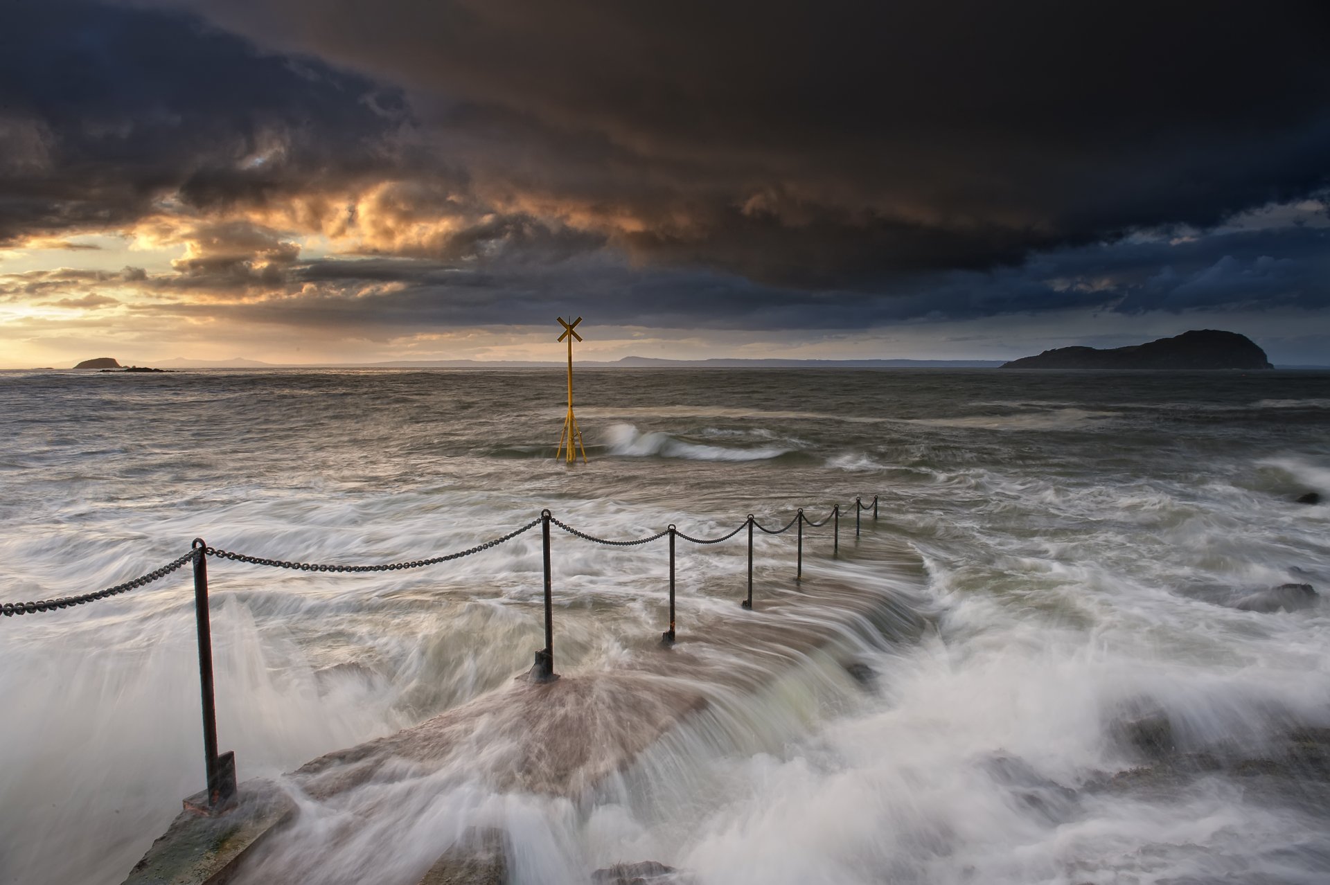 ea ocean bay shore surf waves streams fencing chains pier sign evening sunset sky clouds clouds mountain away