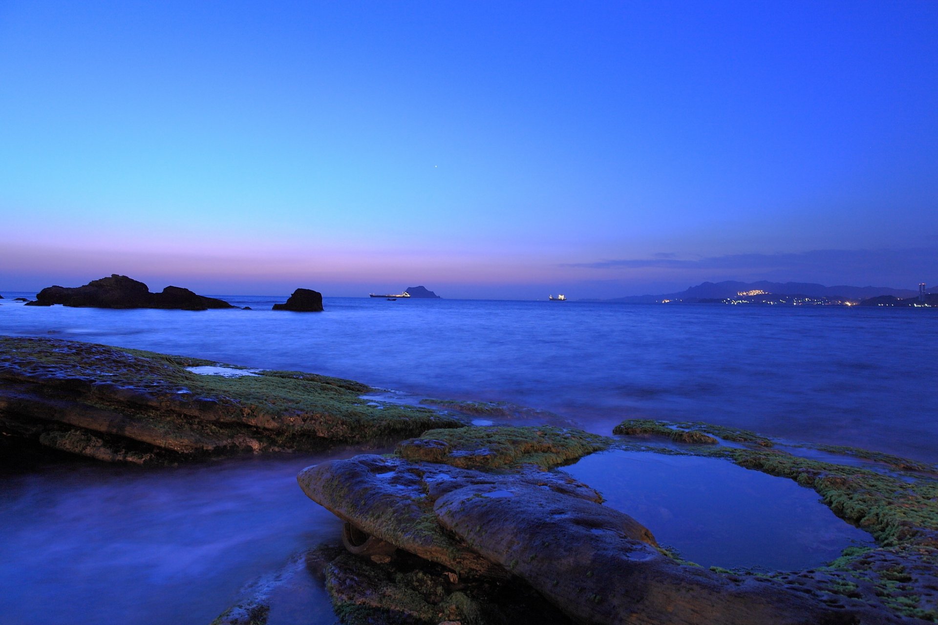 purple night twilight sky blue clouds beach coast sea stones moss away town light