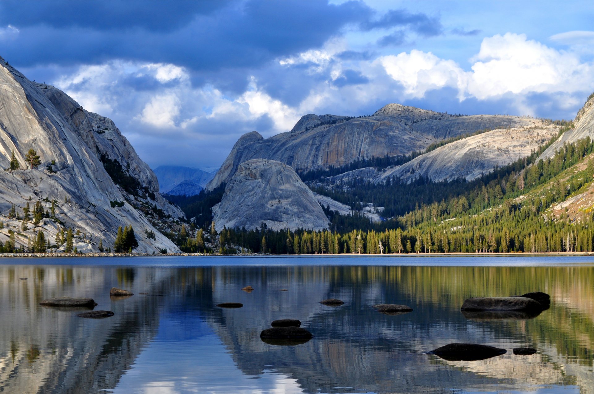 mountains forest trees blue sky clouds clouds lake water smooth surface stones reflection