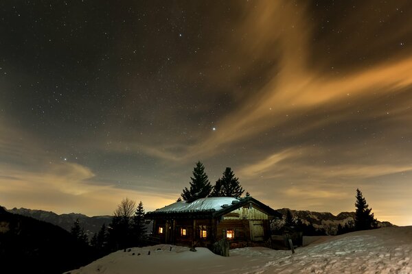 Ein Haus mit brennenden Fenstern in den schneebedeckten Hügeln