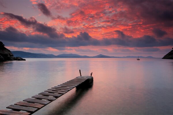 Wooden bridge on the lake. Bright orange sunset