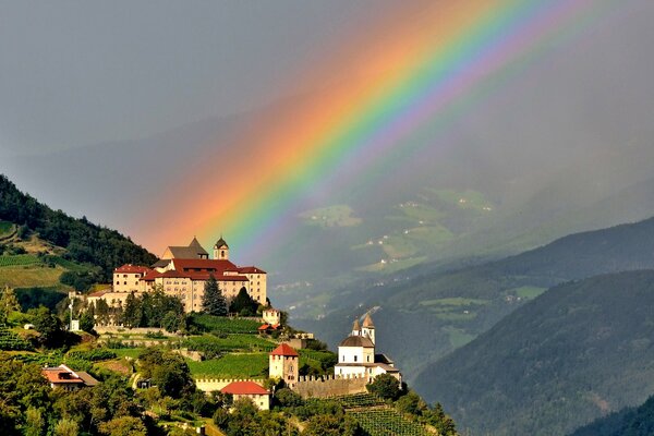 Landschaft mit einem Schloss in den Bergen und einem Regenbogen