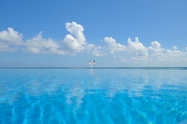 Mar azul claro con yoga que refleja nubes blancas