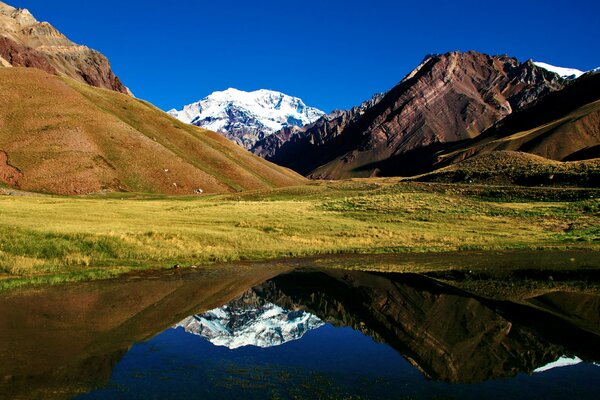 Lago con fondo de montañas y colinas cubiertas de hierba