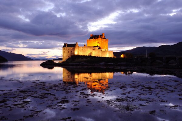 Ein beleuchtetes Schloss in Schottland spiegelt sich im Wasser wider