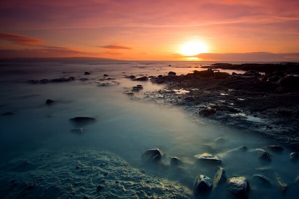 Brillante puesta de sol en la costa con piedras