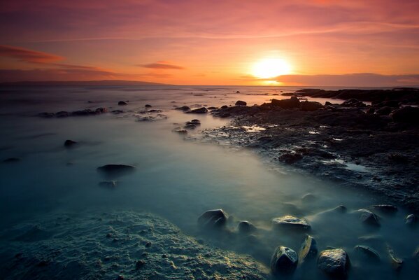 Яркий закат на побережье с камнями
