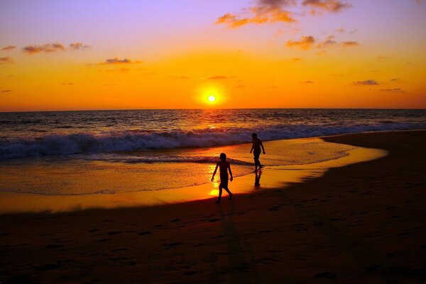 Dos caminan sobre el rojo del sol de la puesta de sol de la arena del mar