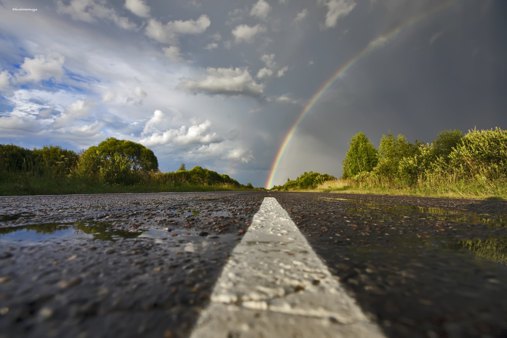 arc-en-ciel route asphalte flaques d eau après la pluie ciel nuages arbres