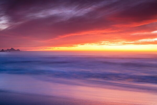 The crimson sunset over the ocean merges with the horizon