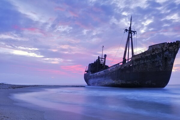 Stary statek na piaszczystej plaży w promieniach zachodu Słońca