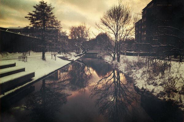 Snowy city in the evening. Bridge on the water