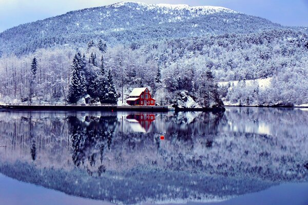 Maison rouge au bord du lac au milieu de la neige