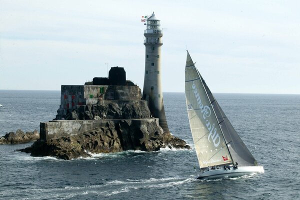 Un yacht navigue devant un phare sur un rocher