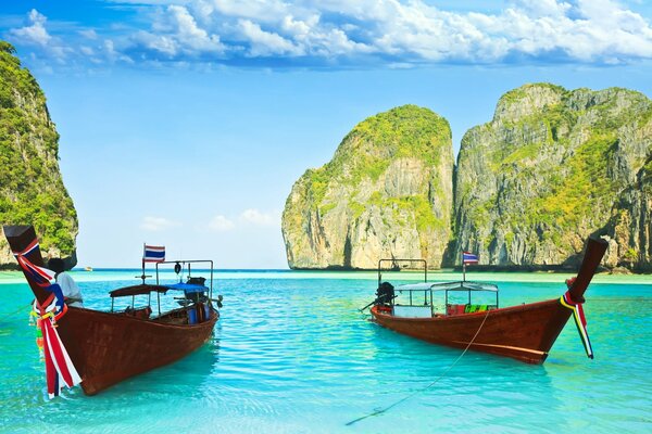 Boats on the turquoise water of the tropical sea against the background of giant rocks and bright sky