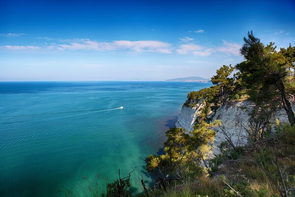 The yacht sails on the sea along the rocks