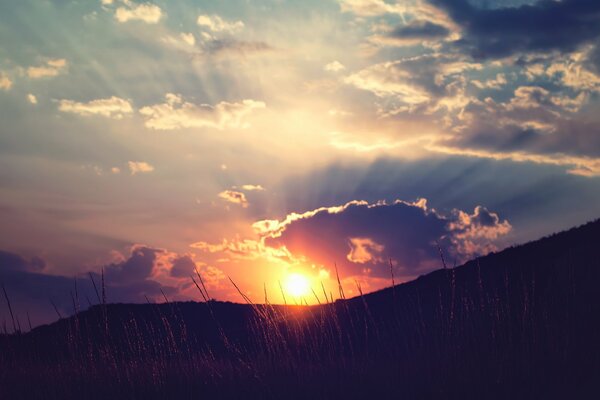 The sun sets in the clouds over the hills