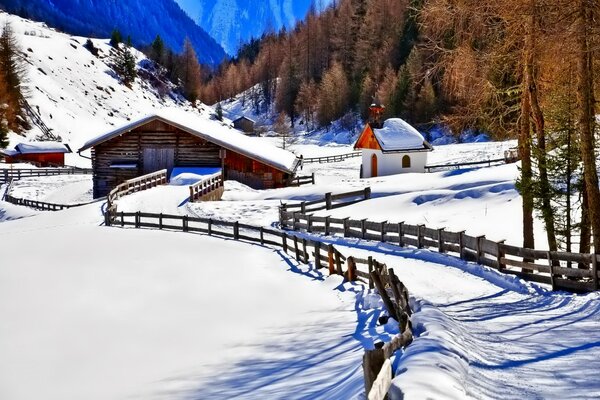 Winter mountains with forest, covered with snow. In the lowlands there are houses with a fenced road