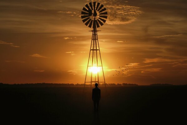 Homme et moulin à vent sur fond de ciel coucher de soleil